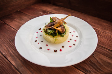 Roasted quail on a bed with mashed potatoes, rocket leaves and berry sauce.   white plate  wooden rustic background. Top view. Close-up