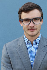 Young handsome man with great smile wearing fashion eyeglasses against neutral blue background