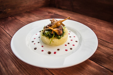 Roasted quail on a bed with mashed potatoes, rocket leaves and berry sauce.   white plate  wooden rustic background. Top view. Close-up