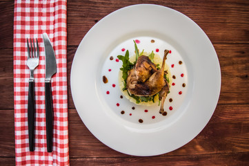 Roasted quail on a bed with mashed potatoes, rocket leaves and berry sauce.   white plate  wooden rustic background. Top view. Close-up