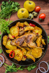 Quail baked in a pan with potatoes and apples. On  brown wooden background. Top view. Close-up