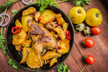 Quail baked in a pan with potatoes and apples. On  brown wooden background. Top view. Close-up