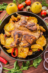 Quail baked in a pan with potatoes and apples. On  brown wooden background. Top view. Close-up