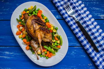 Roasted quail with steamed vegetables. Blue wooden background Top view. Close-up
