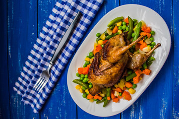 Roasted quail with steamed vegetables. Blue wooden background Top view. Close-up