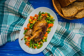 Roasted quail with steamed vegetables. Blue wooden background Top view. Close-up