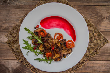 Dish of roasted meat on the grill with berry sauce and arugula in the restaurant. Wooden rustic background. Top view. Close-up