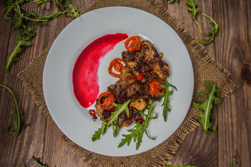Dish of roasted meat on the grill with berry sauce and arugula in the restaurant. Wooden rustic background. Top view. Close-up