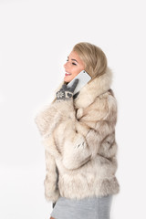 the young woman in a fur coat stands and speaks by phone and smi