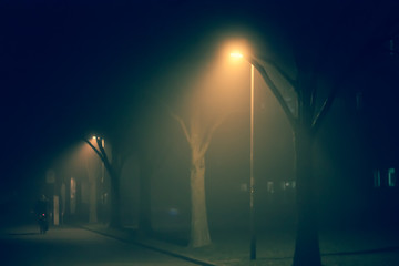 Einsamer Radfahrer nachts auf Straße mit Nebel und Straßenlaternen