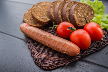 Slice sliced grilled sausage, slices of bread, herbs and cherry tomatoes. top view. wooden black background. Close-up