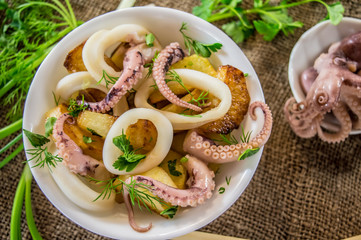 Ready fresh squid rings and tentacles of an octopus with stewed potatoes  greens in rustic. Close-up