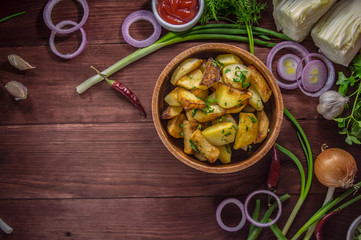 Roasted potatoes with vegetables and herbs on a wooden background, top view. Close-up