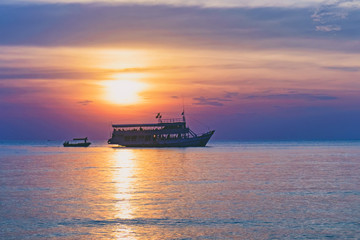 Tropical colorful dramatic sunset with cloudy sky and silhouette of the ship on the horizon. Evening calm on the Gulf of Thailand. Bright afterglow.