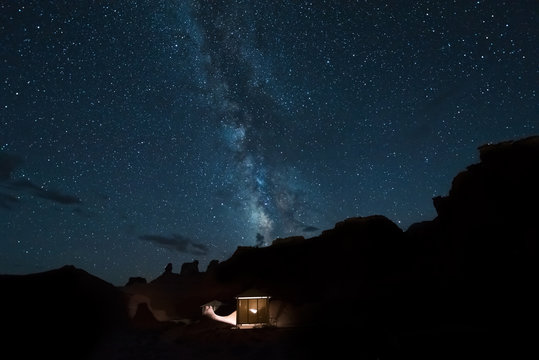 Desert canyons with milky way stars at night and illuminated house