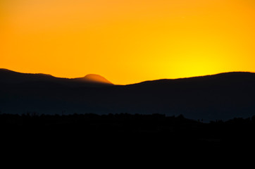 A colorful sunset in Santa Fe, New Mexico with a sun hiding behind mountain