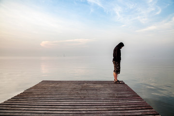 Suicide concept, Depressed young man wearing a black hoodie standing on wooden bridge extended into...