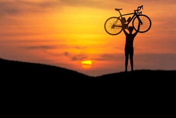 Silhouette the man stand in action lifting bicycle above his head on the meadow with sunset 