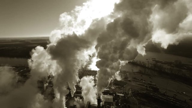 Factory smokestacks, steaming and smoking, stunningly back-lit by the sunrise, breathtaking black and white aerial view.