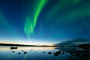 Aurora at Dusk - Banden van bochtige aurora borealis verschijnen direct na zonsondergang boven een noordelijk rotsachtig meer.