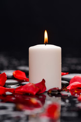 Many rose petals with white candle and therapy stones 