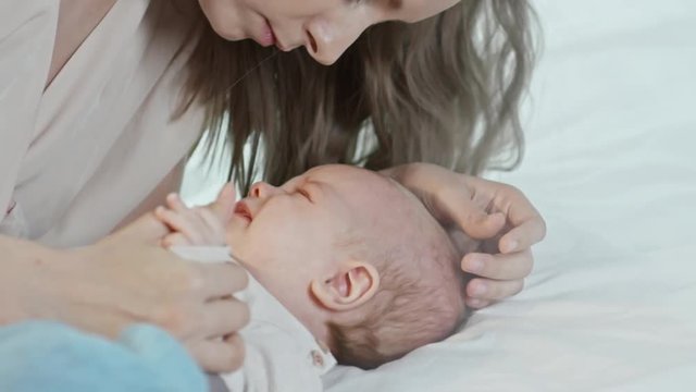 Handheld shot of beautiful young mother kissing forehead of crying baby lying on bed