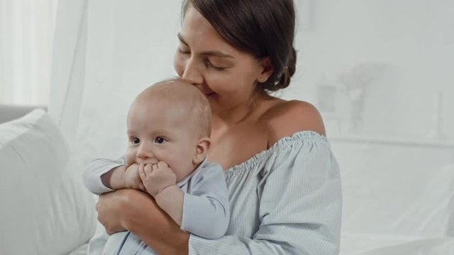 Happy young mother holding adorable little baby boy and posing for camera