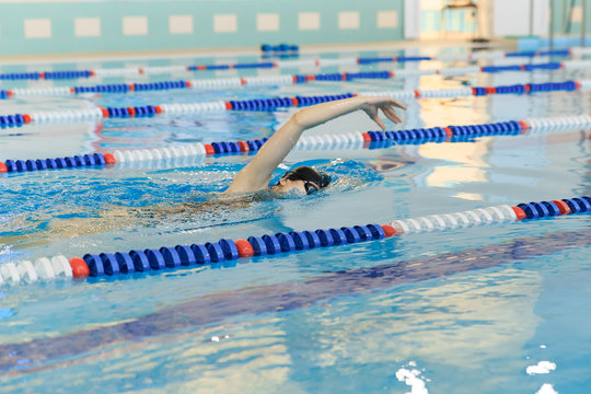 Young woman in goggles and cap swimming front crawl stroke style in the blue water indoor race pool.