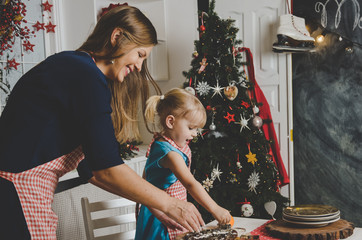 Happy mother and little daughter making Christmas cookies on kitchen