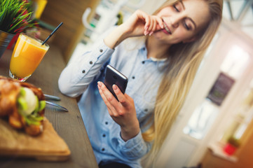 Beautiful woman relaxing in cafe at a table with the phone in hand, checks the social networks on the table orange juice and sweet wafer