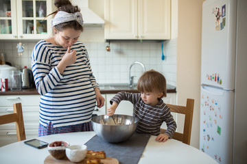 Obraz na płótnie Canvas fun young pregnant mother with son Toddler, make dough for ba