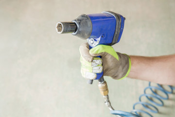 Man's hand in protective glove holding wheel pneumatic wrench in the garage. Seasonal tire change.