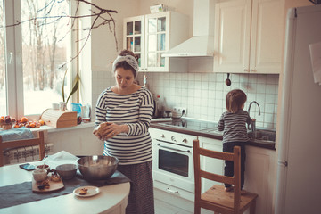 young pregnant mother preparing in kitchen with her son Toddler,
