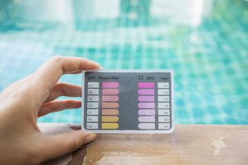 Girl hand holding water testing test kit on swimming pool edge
