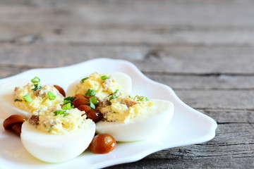 Tasty deviled eggs on a plate and on old wooden background with copy space for text. Hard-boiled eggs stuffed with cheese, marinated mushrooms and fresh green onions. Holiday appetiser recipe. Closeup