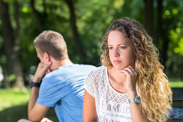 Fototapeta premium Sad young couple sitting on the bench at the park in summer
