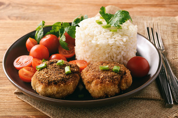 Meat cutlets with boiled rice and tomatoes on wooden background.