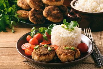 Meat cutlets with boiled rice and tomatoes on wooden background.