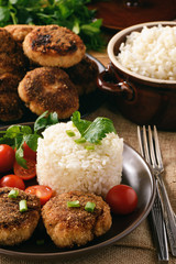 Meat cutlets with boiled rice and tomatoes on wooden background.