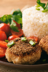 Meat cutlets with boiled rice and tomatoes on wooden background.