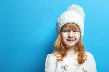 The little red-haired girl posing in a white sweater and hat. The concept of children's fashion, winter.