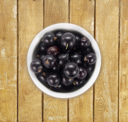 Black currants in a white ceramic bowl. Top view. Ripe and tasty currants on a wooden background.