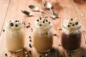 Milk, toffee and chocolate pudding with whipped cream on brown wooden background.