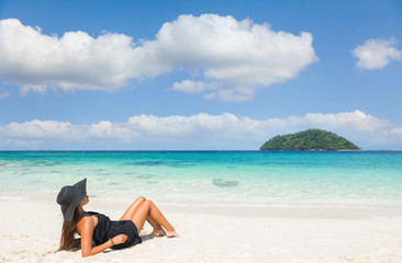 Tropical vacation. Young beautiful woman in black dress and hat on the beach.