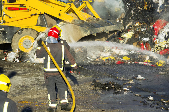 firefighters in industrial warehouse fire working with excavator