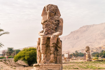 LUXOR: Ancient Colossi of Memnon in Egypt at noon. The original function of the Colossi was to...