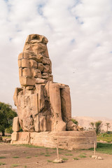 LUXOR: Ancient Colossi of Memnon in Egypt at noon. The original function of the Colossi was to stand guard at the entrance to Amenhotep's memorial temple.