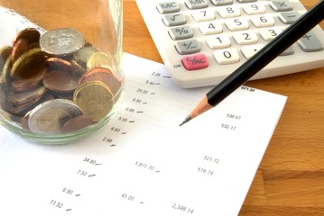 Savings account statement with calculator, pencil, coins and glass jar