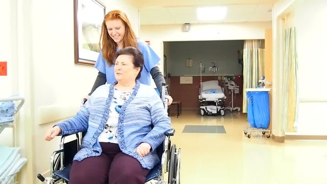 Nurse pushing patient in wheel chair down hallway while talking
