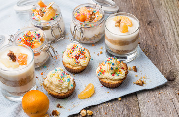 Homemade desserts - biscuits with yogurt, tangerines and walnuts in glass, oats with fresh fruit in glass jar and cupcakes with white frosting and sprinkles.